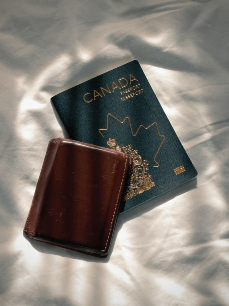 Canadian passport and a leather wallet on white bedsheets