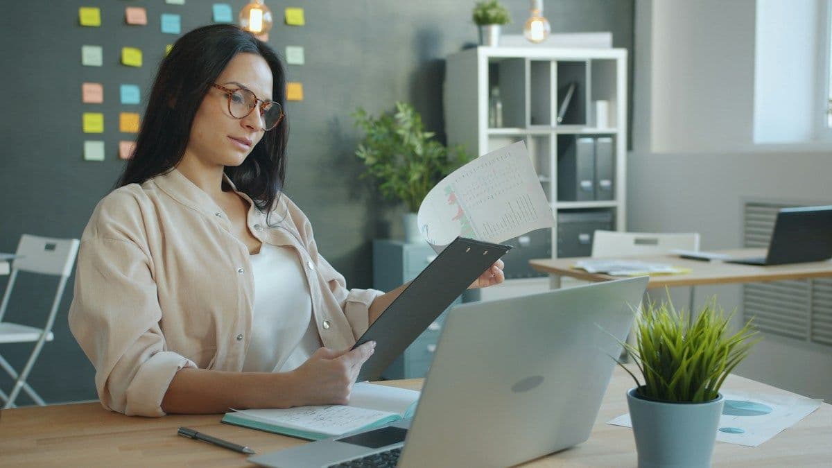 Woman reviewing documents at a desk beside her laptop