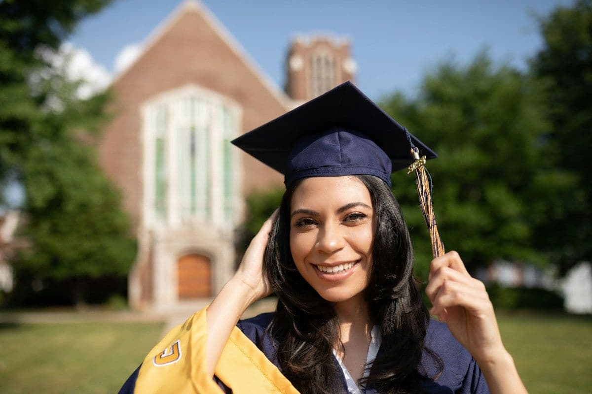 Smiling graduate in cap and gown on a university campus
